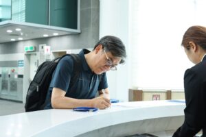 A man signs paperwork at a reception desk.