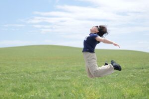 Person happily jumps in a grassy field.